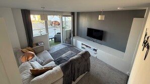 A modern living room with a sofa, a flat-screen TV, and a sliding glass door leading to an outdoor area. - Stylish Marina Apartment with Stunning Views (Portishead)