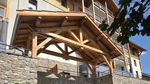 A multi-story building with a wooden balcony structure, stone walls, and a stone entrance.