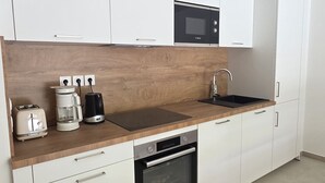 A modern kitchen with white cabinets, a wooden countertop, a built-in oven, a microwave, a coffee maker, and a toaster.