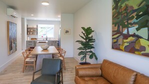 Una sala de estar moderna con un sofá de cuero marrón, un comedor con sillas de madera y una mesa, y un cuadro abstracto grande en la pared.