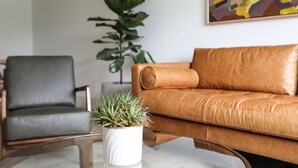 Una sala de estar moderna con un sofá de cuero, un sillón gris, una mesa de centro de vidrio y una planta en maceta.