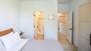 Un dormitorio con una cama, una mesita de noche, un cuadro enmarcado y una puerta que da a otra habitación.