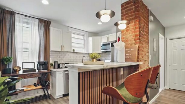 A modern kitchen with a brick accent wall, wooden bar stools, and pendant lighting.