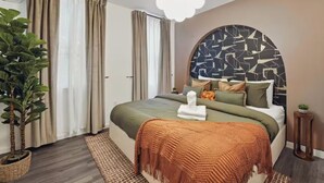 A modern bedroom with a large bed, a round headboard with a geometric pattern, a potted plant, and a hanging light fixture.