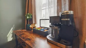 A Keurig coffee maker on a wooden table next to a window with curtains.