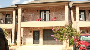 A two-story brick building with a balcony, a garage door, and a red SUV parked in front.