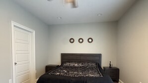 A bedroom with a bed, a ceiling fan, a nightstand, and a door.