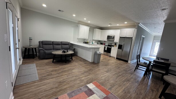 A modern kitchen with white cabinets, stainless steel appliances, and a gray sofa in a living area.