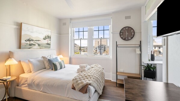 A bedroom with a bed, bedside lamps, a painting, a window with a view, a clock, and a small table. - City Vibes in Darlinghurst (Darlinghurst)
