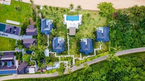 Eine Luftaufnahme eines Resorts mit mehreren bungalowsähnlichen Gebäuden, einem zentralen Pool und einem Strand.