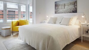 A modern bedroom with a large bed, a yellow chair, and a painting of a snowy landscape.