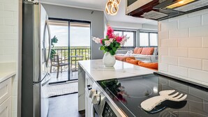 A modern kitchen with a black induction cooktop, a stainless steel refrigerator, and a white marble countertop. - Ocean-View Balcony: Resort Retreat in Myrtle Beach (Myrtle Beach)