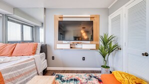 A compact living space with a bed, a small table, a colorful rug, a TV mounted on the wall, and a potted plant. - Ocean-View Balcony: Resort Retreat in Myrtle Beach (Myrtle Beach)
