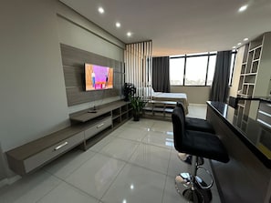 A modern hotel room with a flat-screen TV, a bed, a dining area, and a large window.