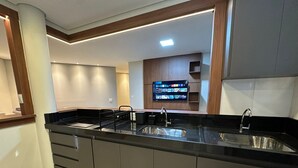Een moderne keuken met een zwart aanrecht, een roestvrijstalen spoelbak en een flatscreen televisie boven de spoelbak.