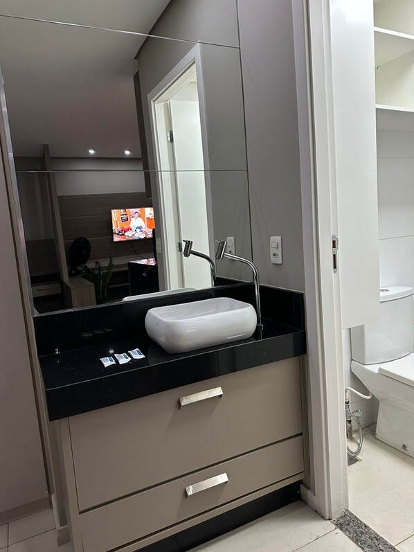 A modern bathroom with a white sink, a mirror, and a black countertop. - Prédio Excelsior (Belo Horizonte)