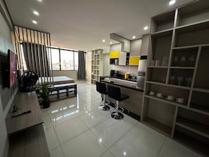 A modern kitchen with a dining area, a TV, and a large window with curtains.