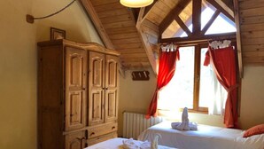 A room with two beds, wooden cabinets, and a window with red curtains.