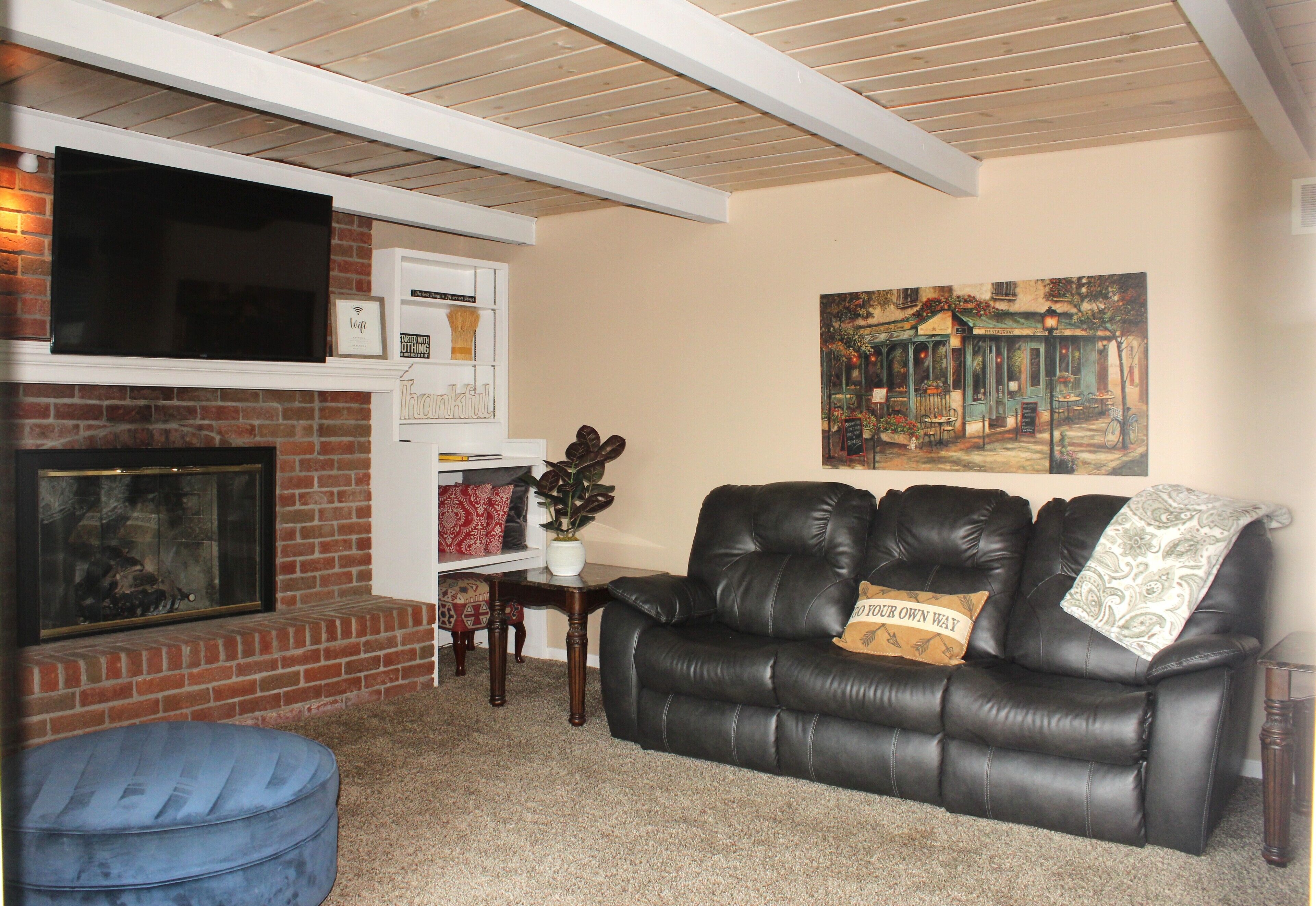 Una sala de estar con chimenea, un sofá de cuero negro y un cuadro en la pared.
