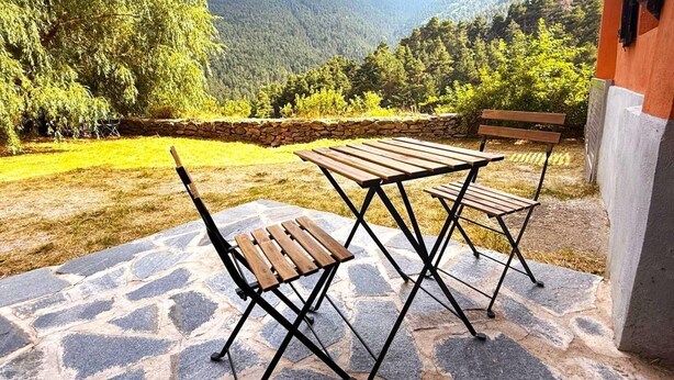 Eine Terrasse im Freien mit Steinboden, Holzmöbeln und Blick auf eine Berglandschaft.