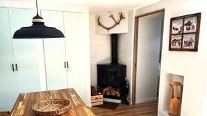 Ein Essbereich mit Holztisch, einer Pendelleuchte, einem Kamin mit Schornstein und einem an der Wand befestigten Hirschgeweih-Dekoration.