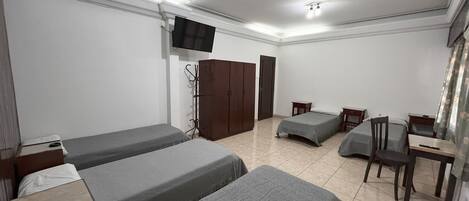 Una habitación con dos camas individuales, un escritorio, una silla, un armario y un televisor montado en la pared.