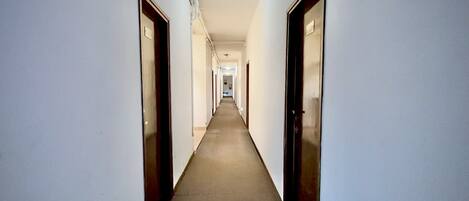 A long, narrow hallway with doors on both sides, leading to a bright room at the end.