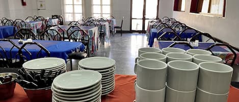 A banquet hall with tables set for an event, featuring stacks of plates and mugs.