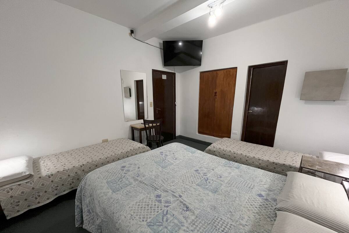 Ein Standard-Hotelzimmer mit zwei Einzelbetten, einem Schreibtisch, einem Sessel, einem an der Wand befestigten Fernseher und einem Kleiderschrank.