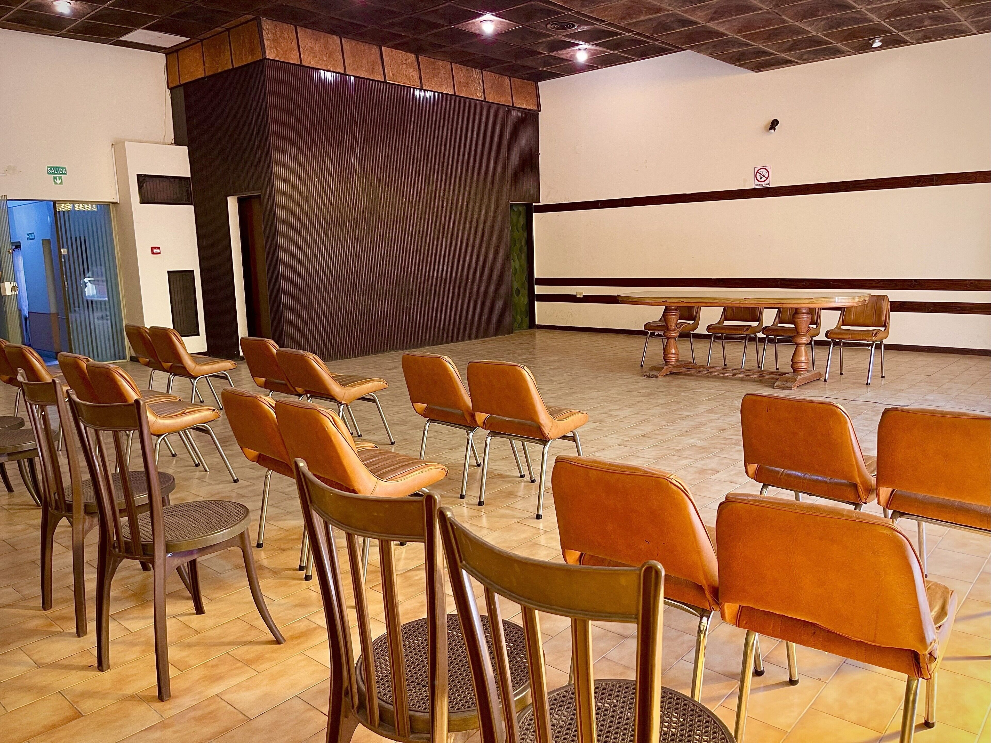 A conference room with rows of chairs, a projector screen, and a wooden table.