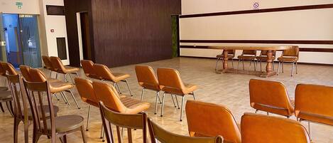Un salón de conferencias con hileras de sillas, una pantalla de proyector y una mesa de madera.