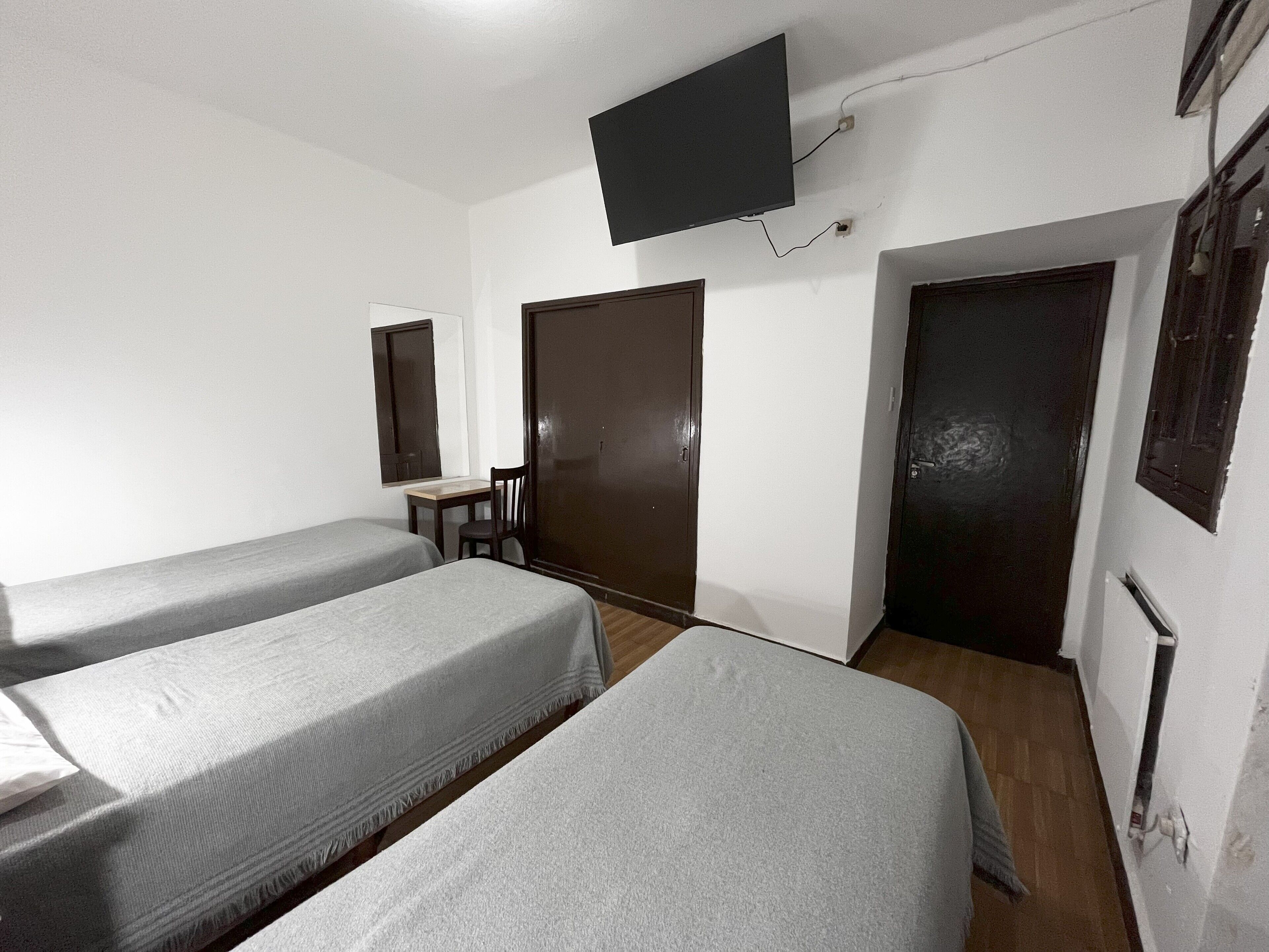 Une chambre d’hôtel avec deux lits simples, un bureau, une chaise, un miroir et un téléviseur fixé au mur.