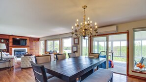 A spacious dining area with a dark wooden table and chairs, a chandelier, and large windows offering a view of the outdoors. - Game Room! Lake-View Gem 7 Mi to Camelback Slopes (Long Pond)