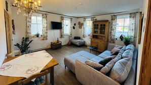 A cozy living room with a sofa, a dining table, and a chandelier. - 60 sqm apartment on the ground floor with garden and courtyard for 2 people (Michelau in Oberfranken)