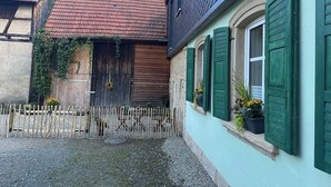 A traditional European courtyard with a wooden gate, a building with green shutters, and a red-tiled roof. - 60 sqm apartment on the ground floor with garden and courtyard for 2 people (Michelau in Oberfranken)