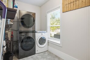 A laundry room with two stacked front-loading washing machines, a drying rack, and a window with blinds. - Hot Tub + Outdoor Kitchen: Stylish Home in Bryan (Bryan)