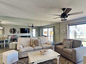 Un salon moderne comprenant un canapé, des fauteuils, une table basse et un ventilateur de plafond.
