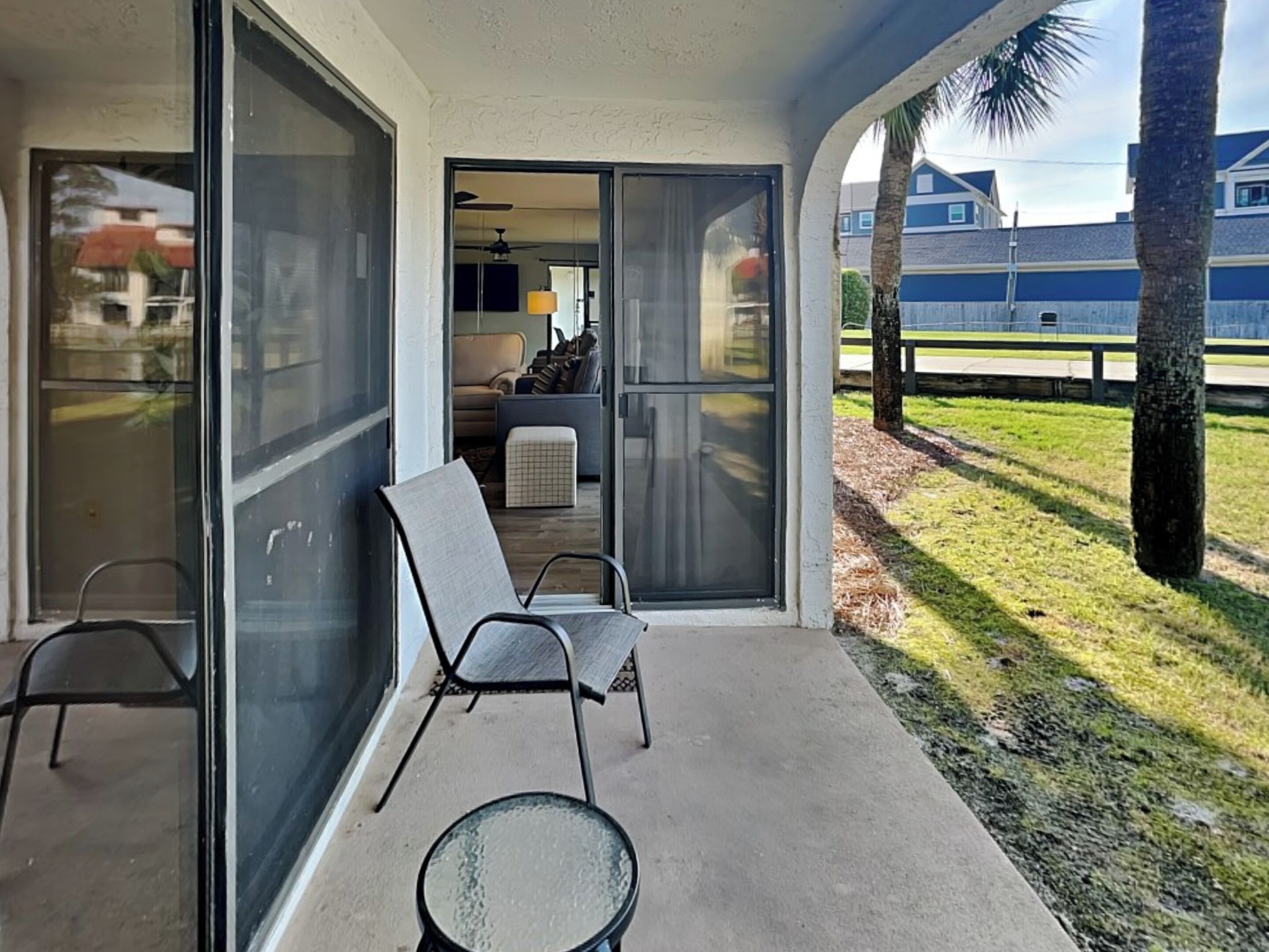 A covered outdoor area with a glass door leading to a living room, a glass table, and two chairs.