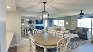 Un soggiorno moderno con zona pranzo, che include un tavolo da pranzo in legno, sedie bianche, un divano grigio e una ventola a soffitto.