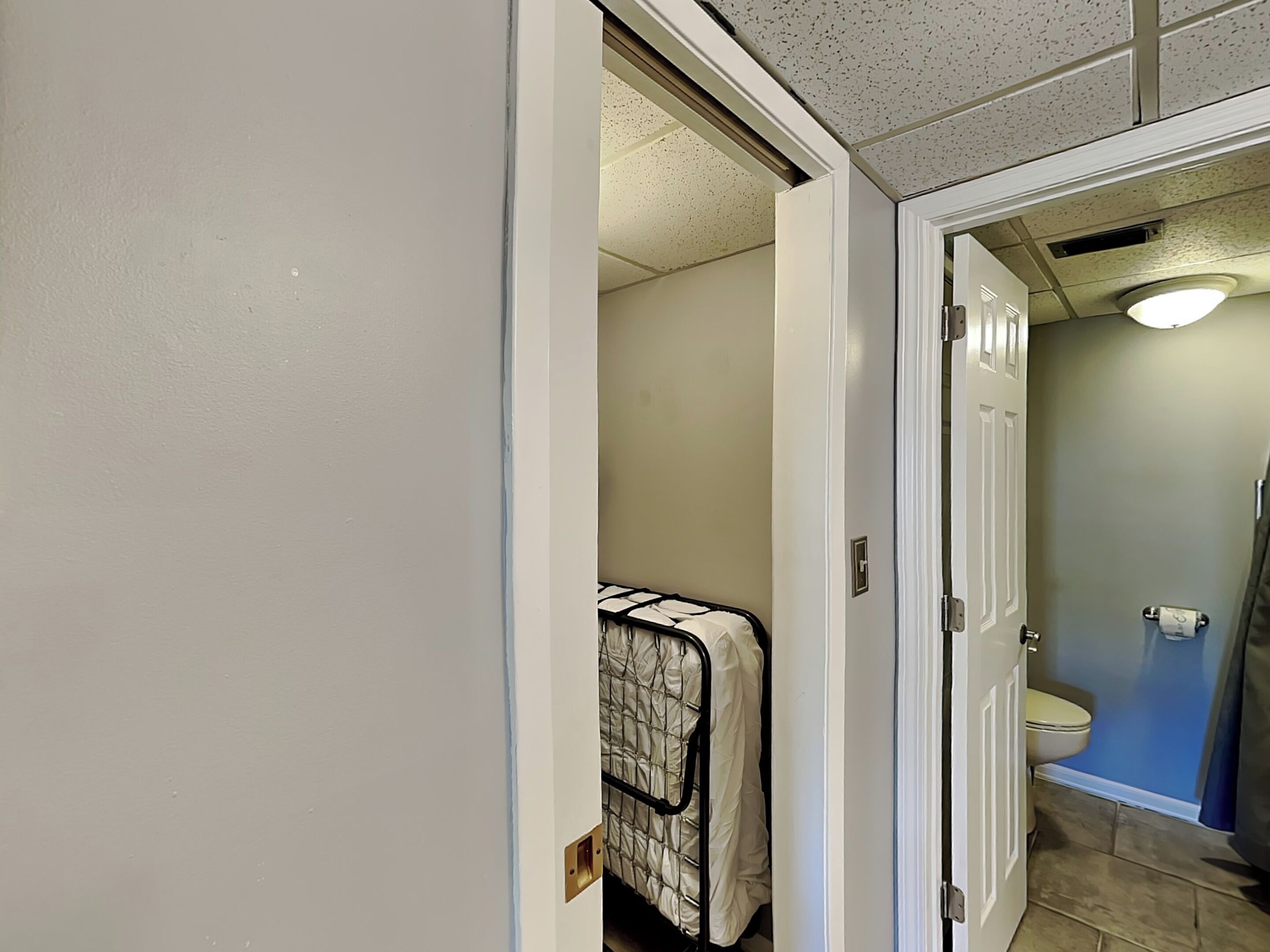 Une salle de bain avec des toilettes, un espace douche et un lit recouvert d’une couvre-lit à motifs.