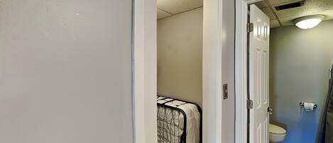 Une salle de bain avec des toilettes, un espace douche et un lit recouvert d’une couvre-lit à motifs.
