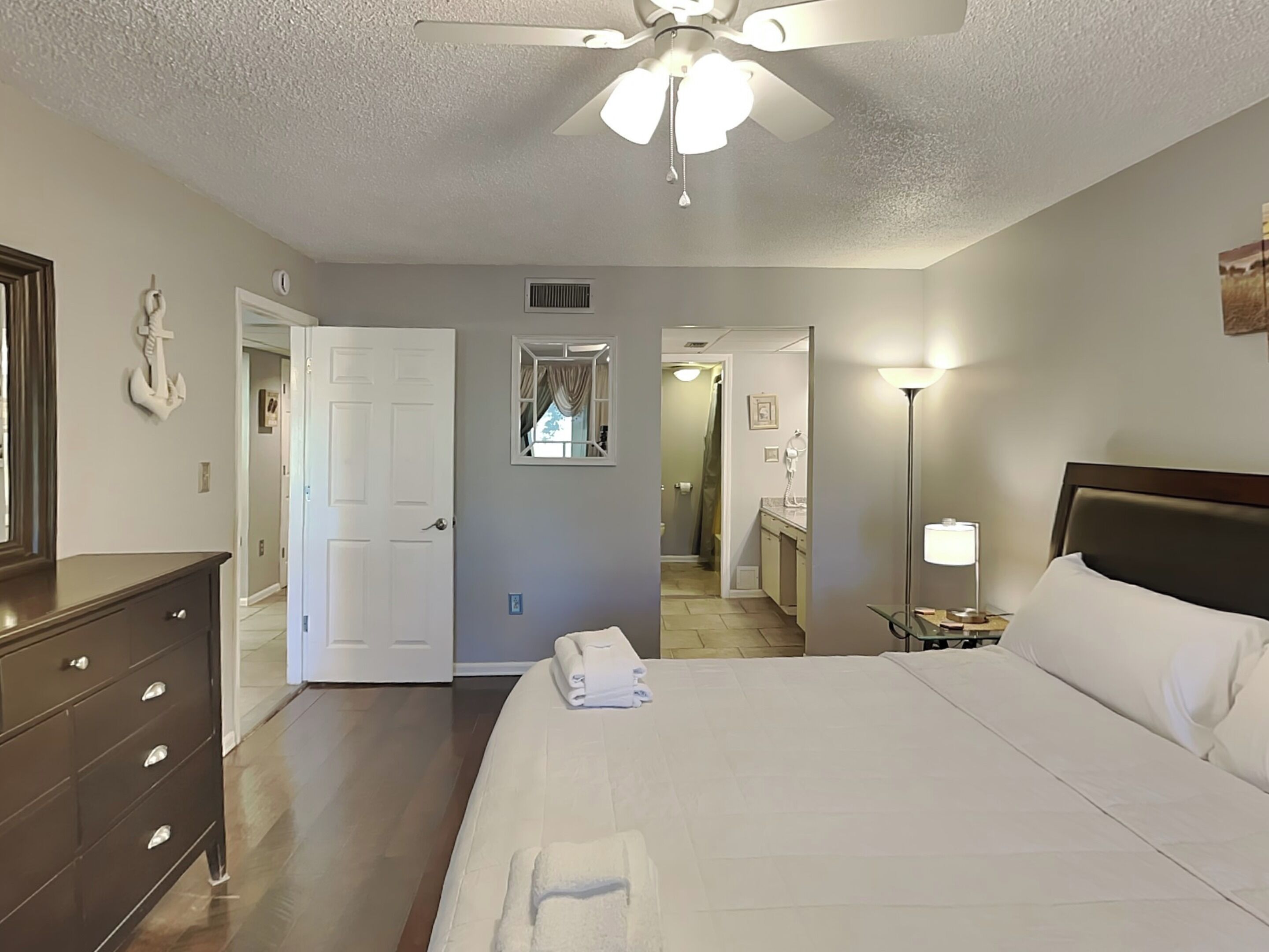 A hotel room with a bed, dresser, ceiling fan, and a bathroom visible through an open door.