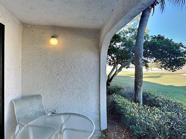 Un patio techado con mesa y sillas, una pared con textura y vista a un campo de golf.