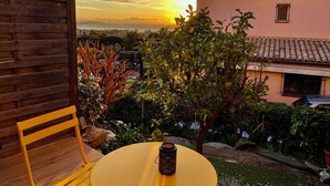 A patio with a yellow table and a wooden chair, overlooking a garden and a pink building with a tiled roof. - Spicy love romantic suite - private jacuzzi - French Riviera - luxury (Villeneuve-Loubet)