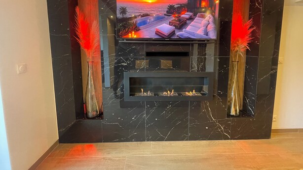 A modern living room with a large flat-screen TV mounted on a black marble wall, flanked by two tall vases with red feathers. - Spicy love romantic suite - private jacuzzi - French Riviera - luxury (Villeneuve-Loubet)