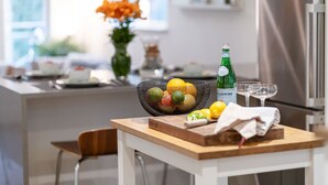 A modern kitchen with a wooden table, a fruit basket, a bottle of Pellegrino water, and a vase with orange flowers. - 2BR Creekside Gem|Steps to Gondola,Free PKNG|Patio (Whistler)
