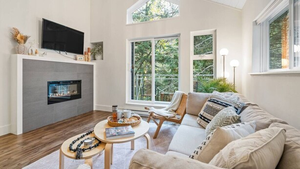 A modern living room with a fireplace, comfortable seating, and large windows offering a view of the outdoors. - 2BR Creekside Gem|Steps to Gondola,Free PKNG|Patio (Whistler)