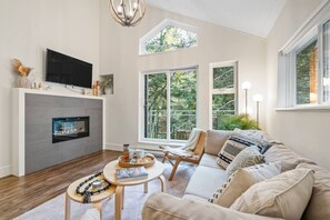 Een moderne woonkamer met een open haard, comfortabele zithoek en grote ramen met uitzicht op de natuur.