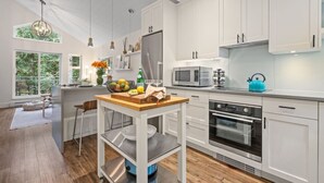 A modern kitchen with white cabinetry, a central island, stainless steel appliances, and a view of the outdoors. - 2BR Creekside Gem|Steps to Gondola,Free PKNG|Patio (Whistler)