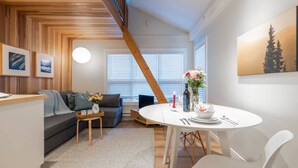 Una sala de estar moderna con techo de madera, un sofá gris, un juego de mesa blanco y una escalera.